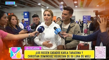Karla Tarazona, con la mano en el abdomen, y Christian Domínguez detrás, atienden a periodistas con micrófonos en un aeropuerto con otras personas.