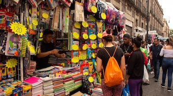 Un puesto callejero muestra pilas de cuadernos, lápices de colores y mochilas colgadas mientras varias personas observan los precios.