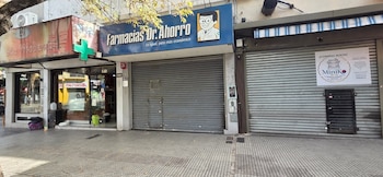 Fachada de una calle urbana. En el centro, Farmacias Dr. Ahorro con persiana metálica gris cerrada. A su derecha, un local con persiana y cartel de MiniKo Korean Market