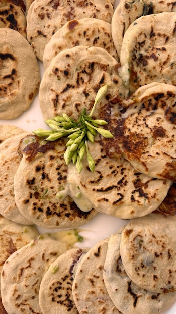 Primer plano de varias pupusas de maíz sobre un plato blanco, algunas con queso derretido y brotes verdes al centro