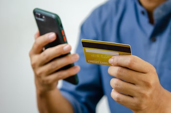 Primer plano de una persona sosteniendo un teléfono móvil con una mano y una tarjeta de crédito dorada en la otra, con una camisa azul
