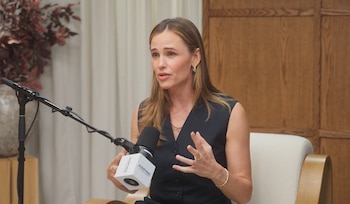 Jennifer Garner viste un chaleco oscuro y gesticula con las manos frente a un micrófono