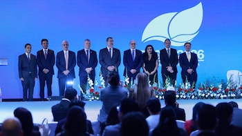 Dos hombres en traje sentados ante una mesa con micrófonos y una pantalla azul que muestra el logotipo de la licitación PEG-6-2026