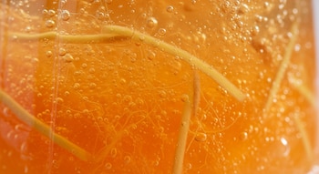 Detalle macro de una gelatina de color naranja vibrante, con numerosas burbujas de aire y finas hebras de jengibre visibles en su interior.