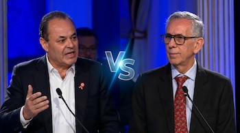 Dos hombres con trajes y corbatas, uno gesticulando en la izquierda y otro con gafas en la derecha, separados por un gráfico brillante que dice 'Vs' sobre un fondo azul.