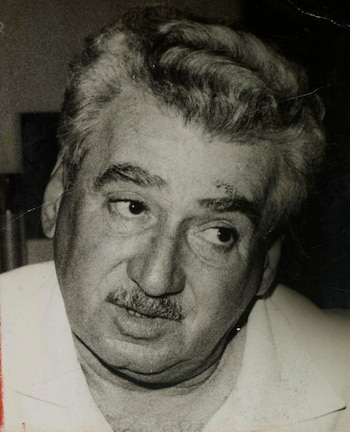 Primer plano de un hombre con cabello oscuro y ondulado, bigote, mirando hacia la derecha. La imagen es en blanco y negro