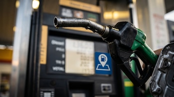 Una boquilla de combustible verde y metálica frente a la pantalla de un surtidor que tiene un ícono azul de ubicación.