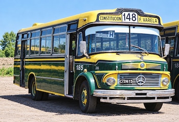 Autobús de colores verde y amarillo con el número 148 y el logotipo de Mercedes-Benz, estacionado sobre un suelo de tierra