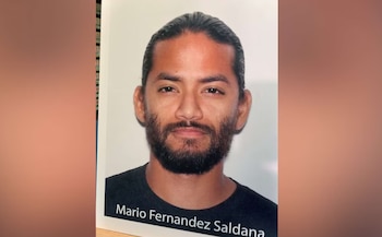 Retrato de un hombre con pelo oscuro recogido hacia atrás, barba, bigote y camiseta negra. Su nombre, Mario Fernandez Saldana, aparece en la parte inferior