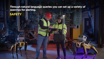 Dos personas con chalecos reflectantes y cascos de seguridad observan una tableta, flanqueadas por dos robots amarillos y negros con forma de perro en una planta industrial