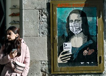 Detalle de la imagen del artista callejero que muestra a la Gioconda con mascarilla y un teléfono móvil en el centro de Barcelona.