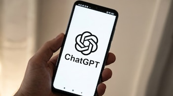 Una mano sostiene un smartphone de color oscuro con la pantalla encendida mostrando el logo negro de ChatGPT y el texto 'ChatGPT' sobre un fondo blanco.