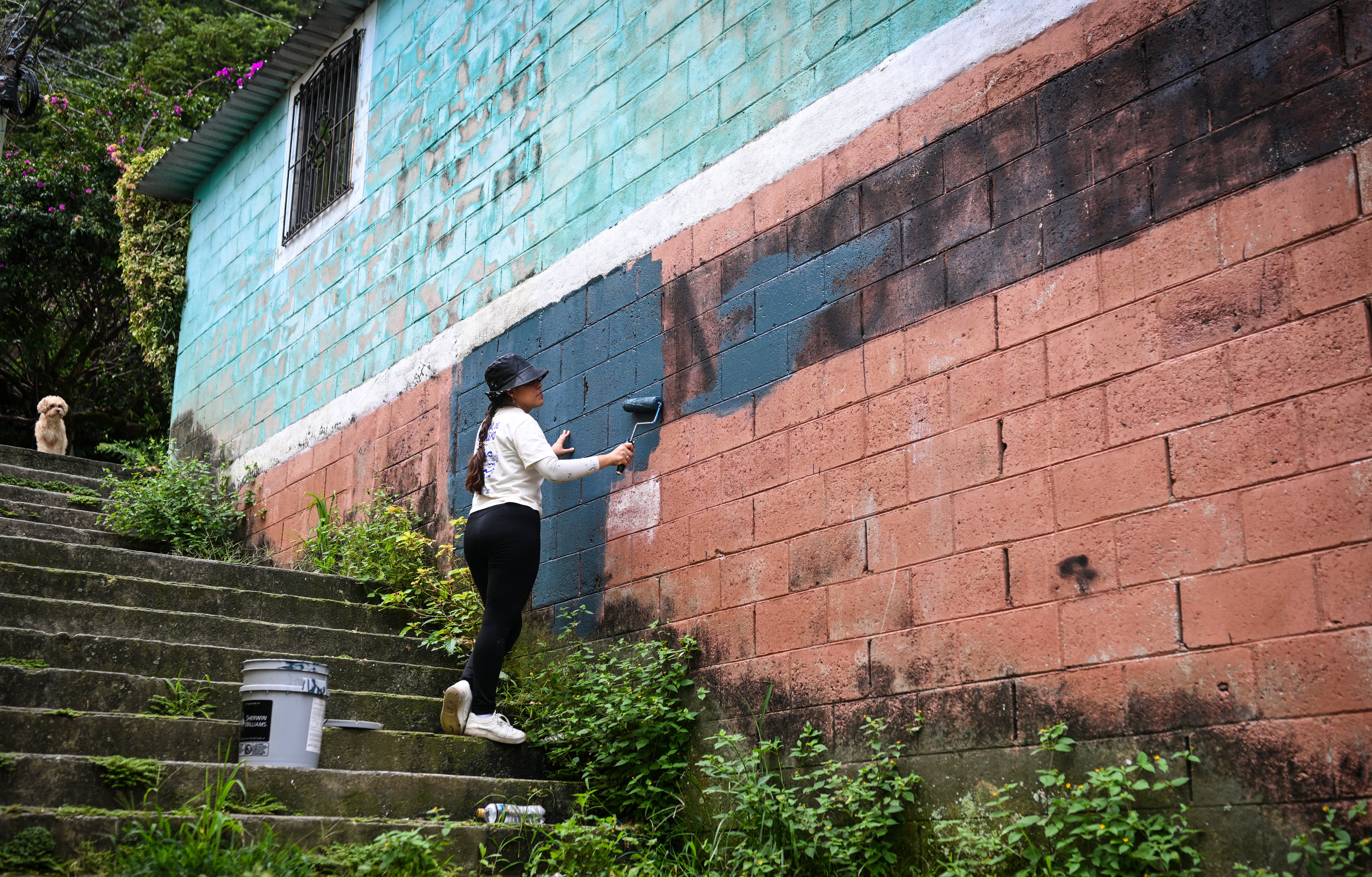 La artista salvadoreña Elizabeth Guardado borra un mural que representa a la pandilla MS (Mara Salvatrucha) antes de la creación de una nueva obra de arte como parte de un festival de arte urbano en la comunidad 10 de Octubre de San Marcos, El Salvador, el 2 de octubre de 2026. El proyecto artístico busca transformar la identidad de una comunidad históricamente afectada por la violencia de las pandillas. (Foto de Marvin RECINOS / AFP)