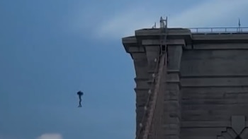 Cielo azul; una torre de puente gris; una figura oscura de forma humana suspendida en el aire