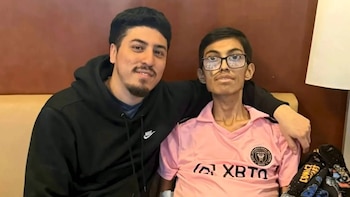 Dos hombres sonríen a la cámara; uno, con sudadera Nike, abraza al otro, más joven, con gafas y una camiseta rosa del Inter Miami CF