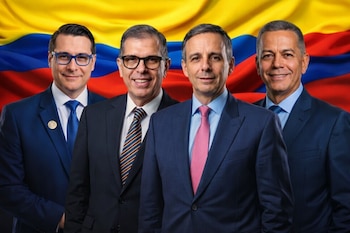 Cuatro hombres vestidos con traje y corbata sonríen de frente. Detrás de ellos se observa una bandera de Colombia en amarillo, azul y rojo.