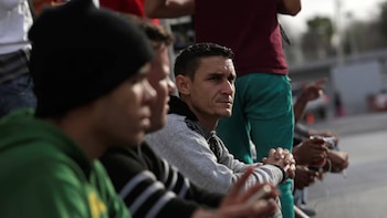 Primer plano de un hombre con sudadera gris y pelo corto, mirando atentamente hacia la derecha, con otras personas borrosas en la multitud
