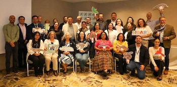 Grupo de personas sonriendo, algunas sentadas y otras de pie, sostienen figuras de animales y plantas, y carteles de CONAP, GUATEMALA, SIGAP
