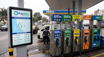 Pantalla informativa con mapa junto a varios surtidores de combustible rotulados con precios en una estación de servicio.