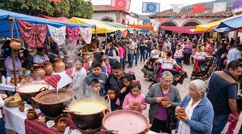 Un mercado festivo al aire libre con toldos coloridos, una multitud, grandes ollas de barro humeantes de atole y personas bebiendo en tazas de barro.