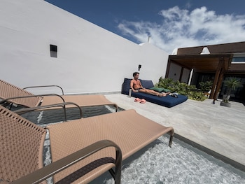 Un hombre sin camiseta descansa en un sillón azul junto a la piscina de una residencia moderna