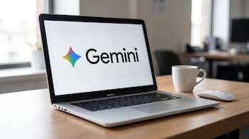 Un MacBook plateado abierto sobre un escritorio de madera muestra el logo de Gemini en su pantalla blanca. A su lado derecho, una taza blanca y un ratón.