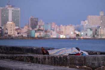 Una persona duerme envuelta en una sábana sobre el muro del malecón al amanecer en La Habana, el 13 de agosto de 2026. Muchos cubanos duermen al aire libre durante las noches de verano en busca de alivio ante las altas temperaturas y los frecuentes cortes de electricidad (Yamil Lage/AFP)