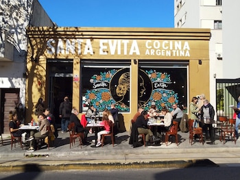 Fachada de un restaurante con el letrero Santa Evita Cocina Argentina y personas sentadas a mesas en la acera