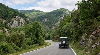 Vista desde atrás de un todoterreno verde sobre una carretera asfaltada de carril único rodeada de laderas boscosas.