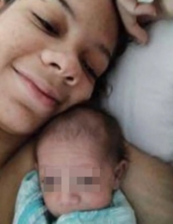 Mujer con ojos cerrados y sutil sonrisa, recostada junto a un bebé envuelto en manta blanca y azul. La cara del bebé está pixelada