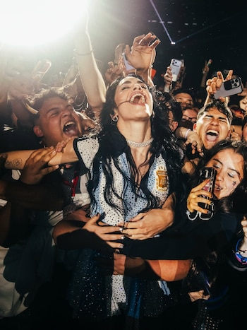 La cantante Lali Espósito, con camiseta de Argentina, sonríe con la boca abierta y los ojos cerrados, abrazada por fans eufóricos en un concierto