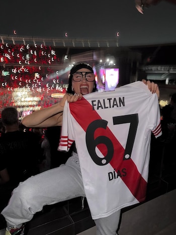 Lali Espósito, con gafas y gorra, sonríe y sostiene una camiseta de River Plate que dice "Faltan 67 días" en un estadio iluminado