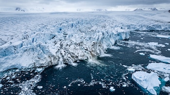 Vista aérea de un glaciar agrietado con cascadas que desembocan en el mar junto a témpanos de hielo.