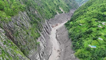 Vista aérea de un cañón profundo rodeado de laderas verdes con un lecho cubierto de barro gris y sedimentos