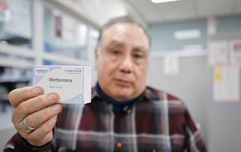 Hombre con camisa a cuadros sostiene una caja blanca de "Metformina Tableta 850 mg" que dice "Propiedad del Sector Salud"