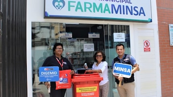 Tres personas posan frente a una farmacia "FARMAMINSA" junto a un contenedor rojo para medicamentos; dos llevan letreros de DIGEMID y MINSA