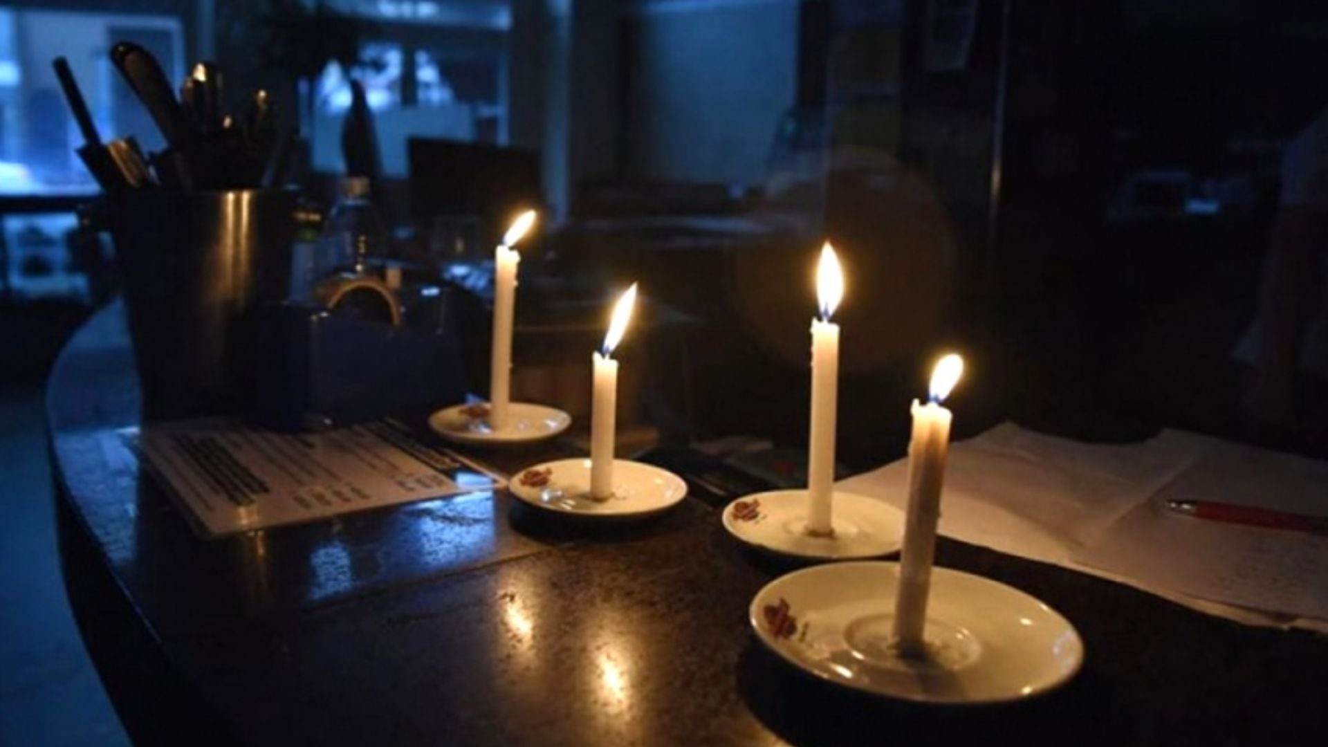 Cuatro velas encendidas sobre una mesa de madera oscura iluminan el ambiente durante un corte de luz en Lima. (Imagen Ilustrativa Infobae)