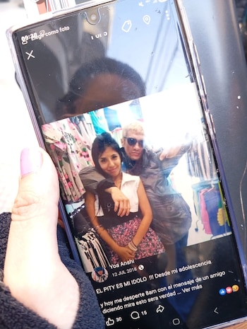 Mano de mujer con uña pintada sujeta un teléfono móvil que muestra una pantalla con una foto de un hombre y una mujer joven en una tienda de ropa