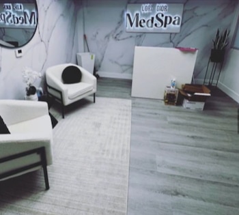 Dos sillones blancos con cojines negros, una alfombra clara, un mostrador de recepción y un cartel iluminado en la pared