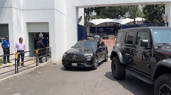 Una camioneta negra Mercedes-Benz transita por una puerta de acceso junto a un vehículo Jeep y dos hombres con uniforme.