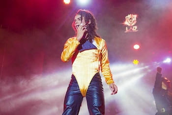 Gabriela Villanueva, imitadora de Michael Jackson, en el escenario, vistiendo un top dorado y pantalones oscuros, con luces rojas y humo de fondo