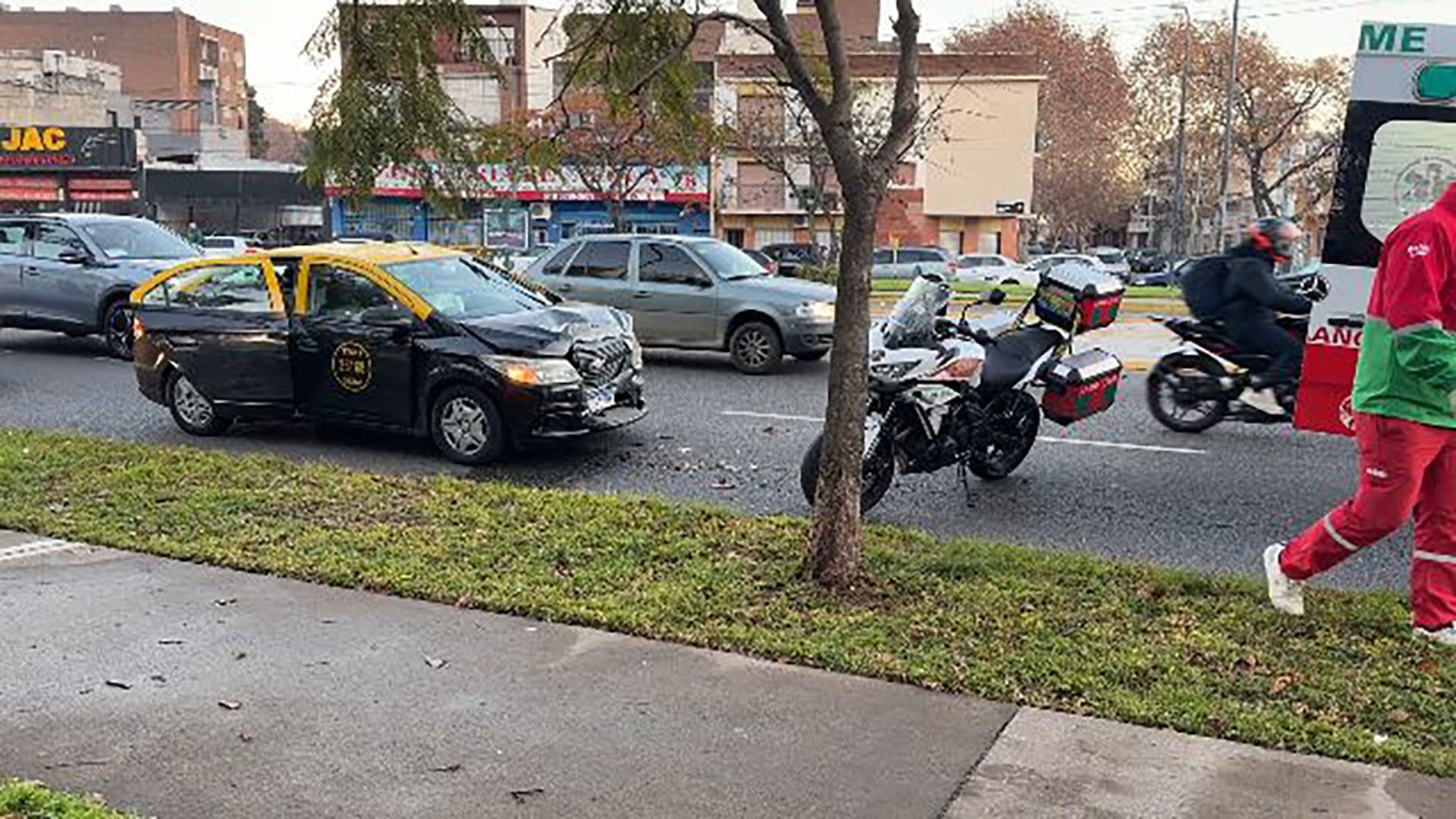 Un taxi con daños frontales y una puerta abierta se encuentra en Avenida Juan B. Justo tras un accidente vehicular, con una ambulancia presente en el lugar.