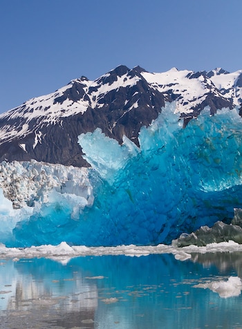 Vista panorámica de un imponente glaciar azul brillante que se encuentra con un lago de aguas tranquilas, rodeado de montañas nevadas bajo un cielo claro