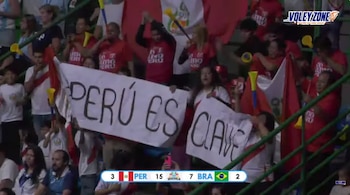 Espectadores en la tribuna sostienen una pancarta blanca con el texto PERÚ ES CLAVE durante un partido de voleibol entre Perú y Brasil