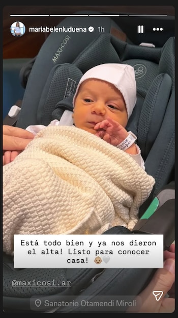 Primer plano de un bebé recién nacido, Vito, con gorro blanco y envuelto en una manta beige, sentado en un asiento de seguridad para coche gris oscuro