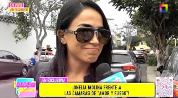 Primer plano de Onelia Molina con gafas de sol oscuras, labios fruncidos y pelo negro liso, siendo entrevistada con un micrófono en una calle