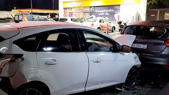 Dos coches chocados de noche. El vehículo blanco tiene el frente muy dañado, mientras que el gris oscuro muestra impacto trasero. Vidrios rotos en el suelo