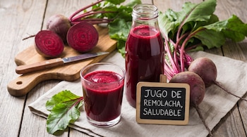 Remolachas enteras y en mitades, cuchillo en tabla de madera. Vaso y botella de jugo de remolacha. Letrero con "Jugo de remolacha, saludable".