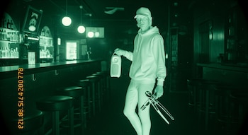 Interior de un bar con poca luz; un hombre con gorra, buzo y pantalones ajustados sostiene un parlante y unos alicates; imagen verde granulada con sello de tiempo.