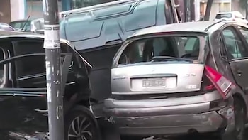 Vehículos de color gris y negro dañados en la vía pública con abolladuras y cristales rotos